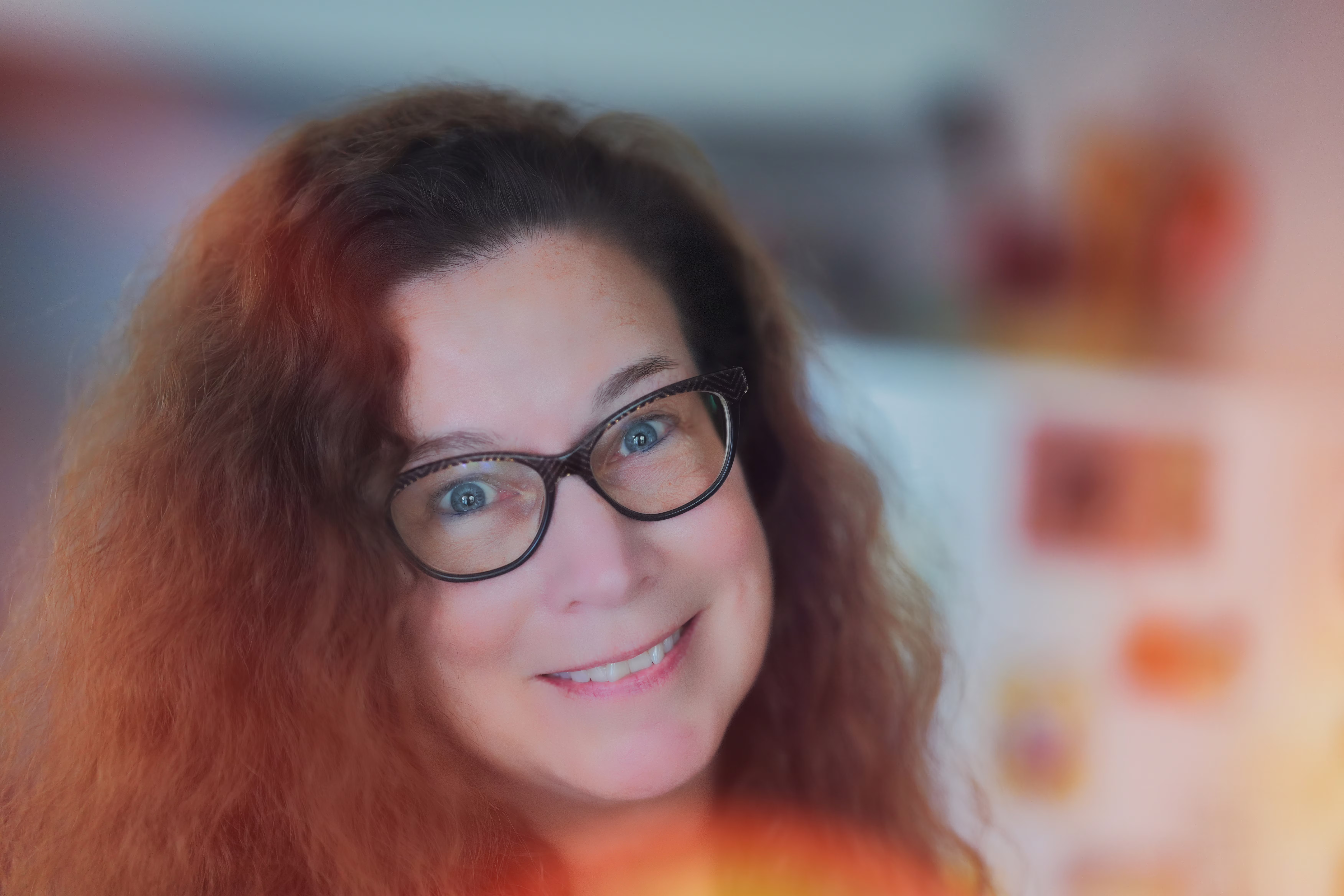Close-up portrait of a smiling woman with red hair and glasses in warm light